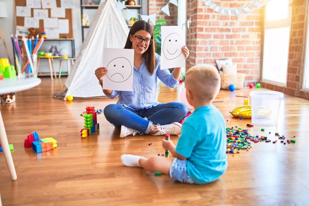 A Woman Holding A Smiley Face and A Sad Face — Oracle Psychology Child & Adolescent Psychologists Newcastle in Newcastle, NSW