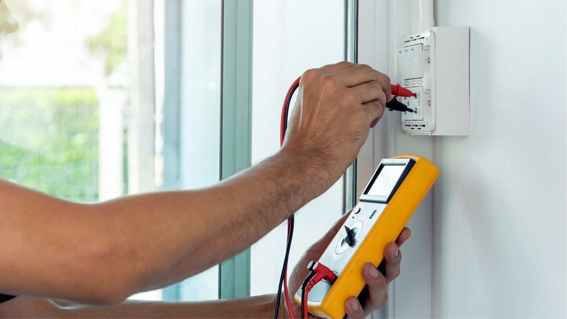 A man is using a multimeter to test an electrical outlet.
