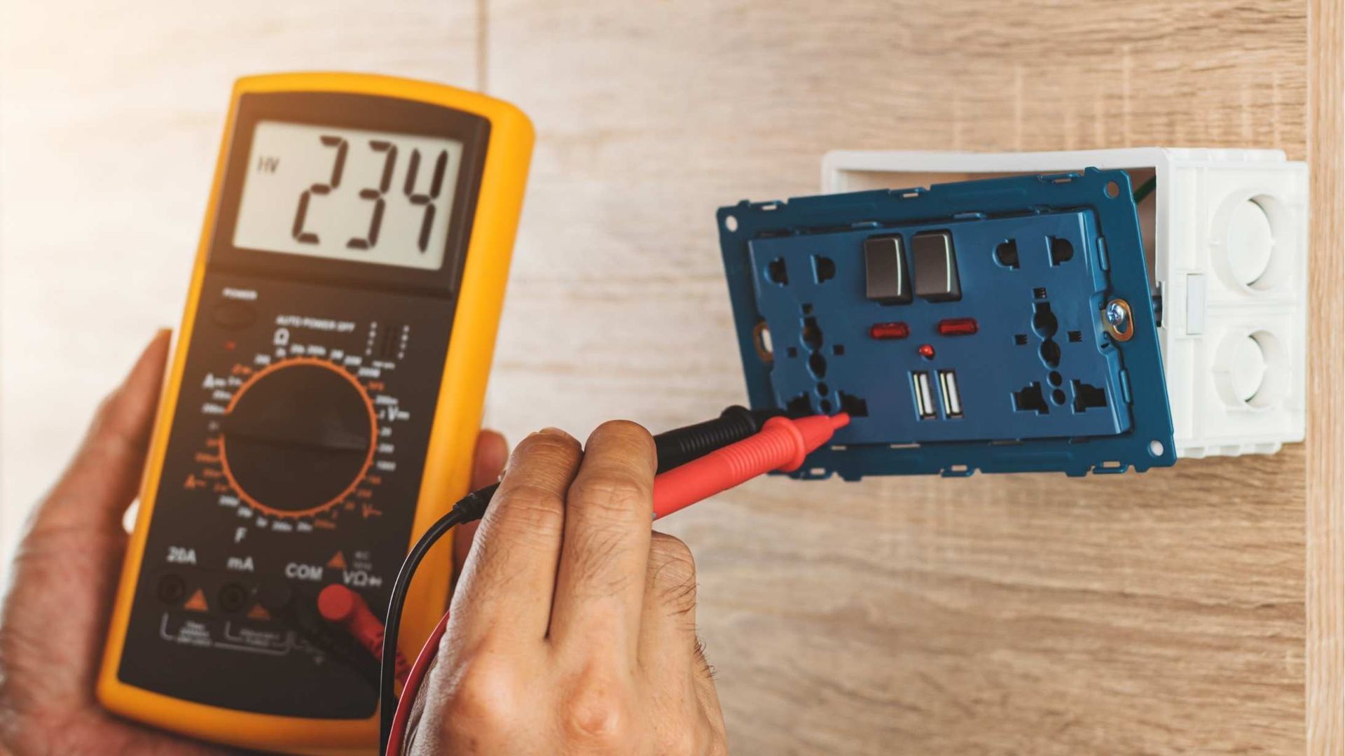 A person is using a digital multimeter to test an electrical outlet.
