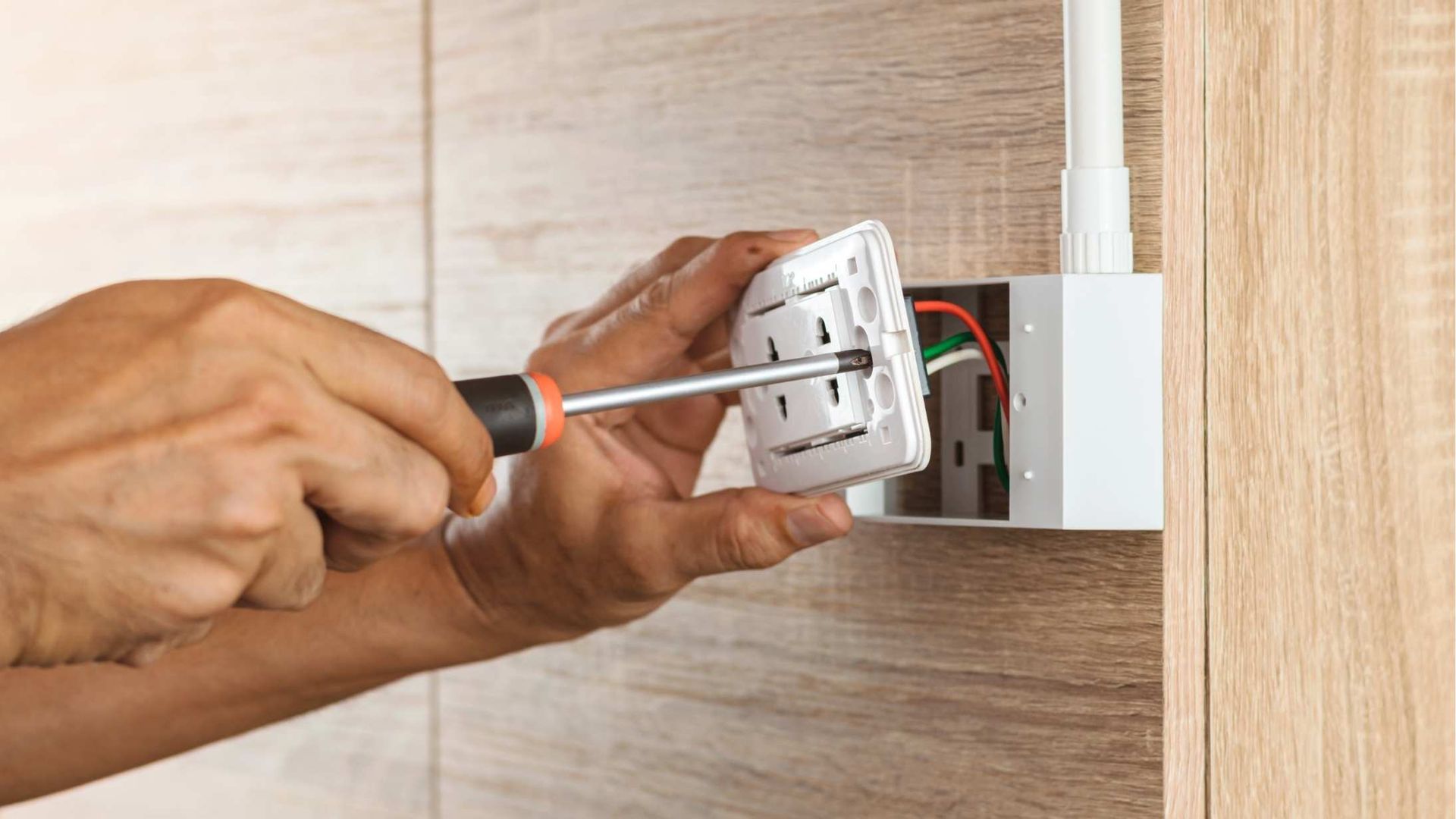 A person is fixing an electrical outlet with a screwdriver.