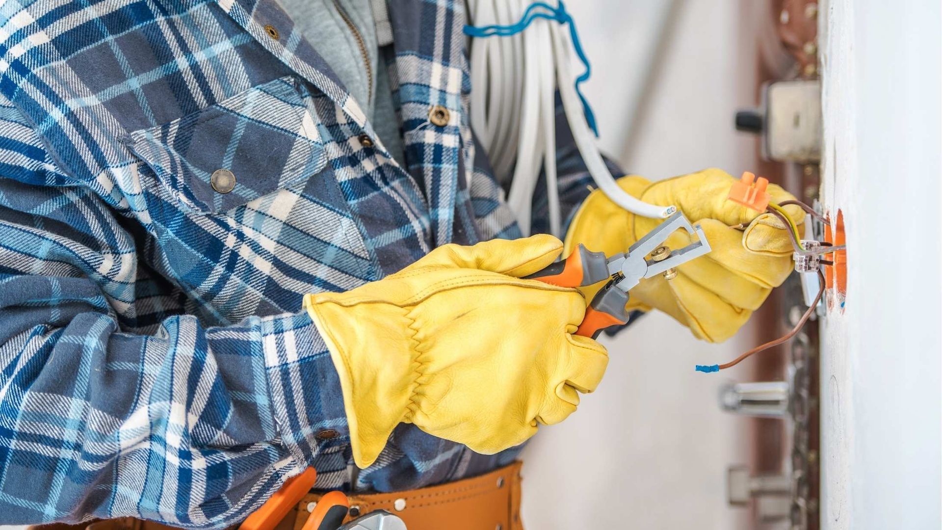 A man in a plaid shirt and yellow gloves is working on an electrical outlet.