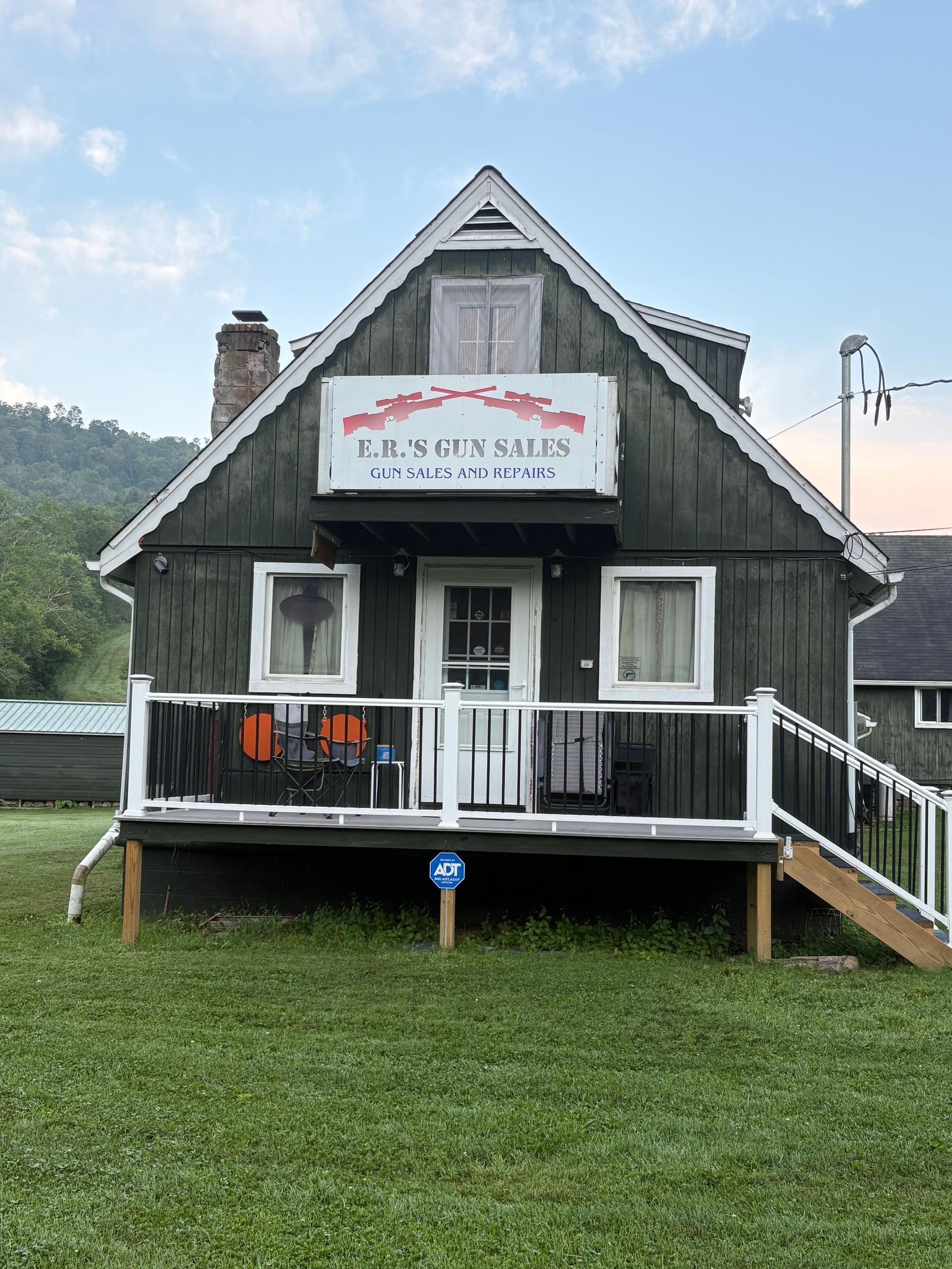 A small black house with a white porch and stairs is sitting on top of a lush green field.