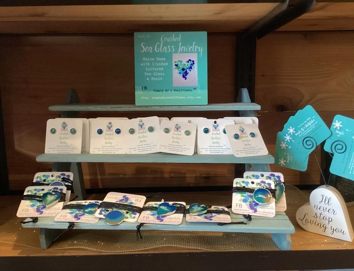 A display of sea glass jewelry is on a wooden shelf.