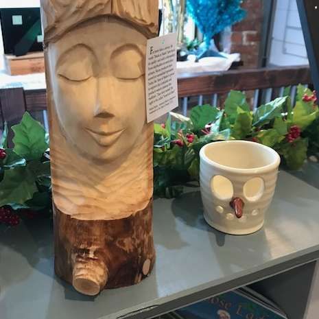 A wooden statue of a woman 's head is sitting on a table next to a ceramic cup.