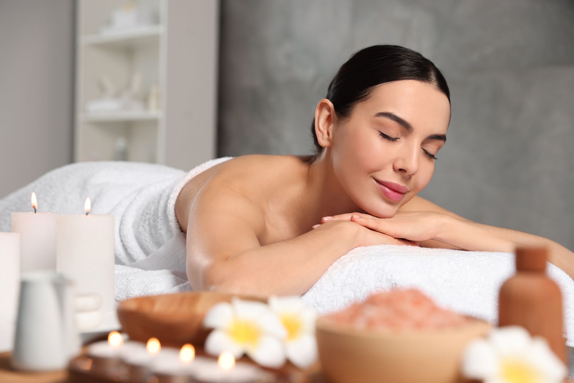 A woman is laying on a massage table in a spa with candles and flowers.