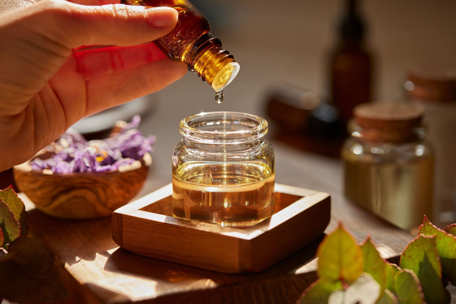 A person is pouring essential oil into a glass jar