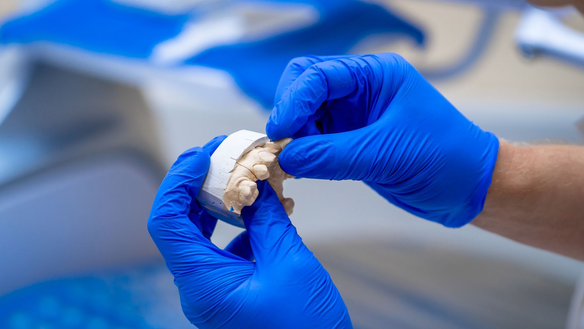 Dentist's gloved hands examining a dental mold in a dental office setting.