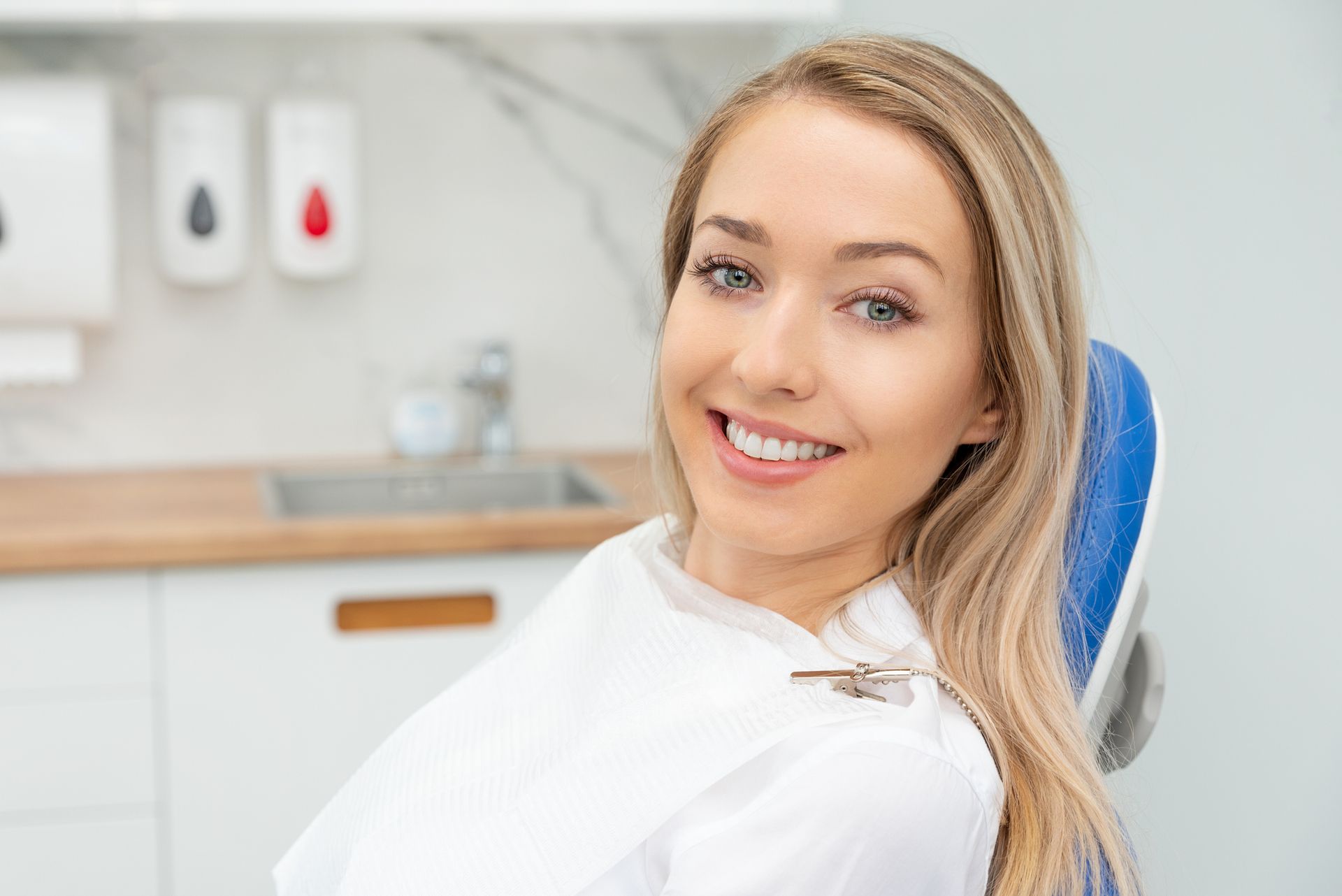 Woman smiles in a dental chair, white bib, clinic interior, blonde hair. Woman smiles in a dental chair, white bib, clinic interior, blonde hair.
