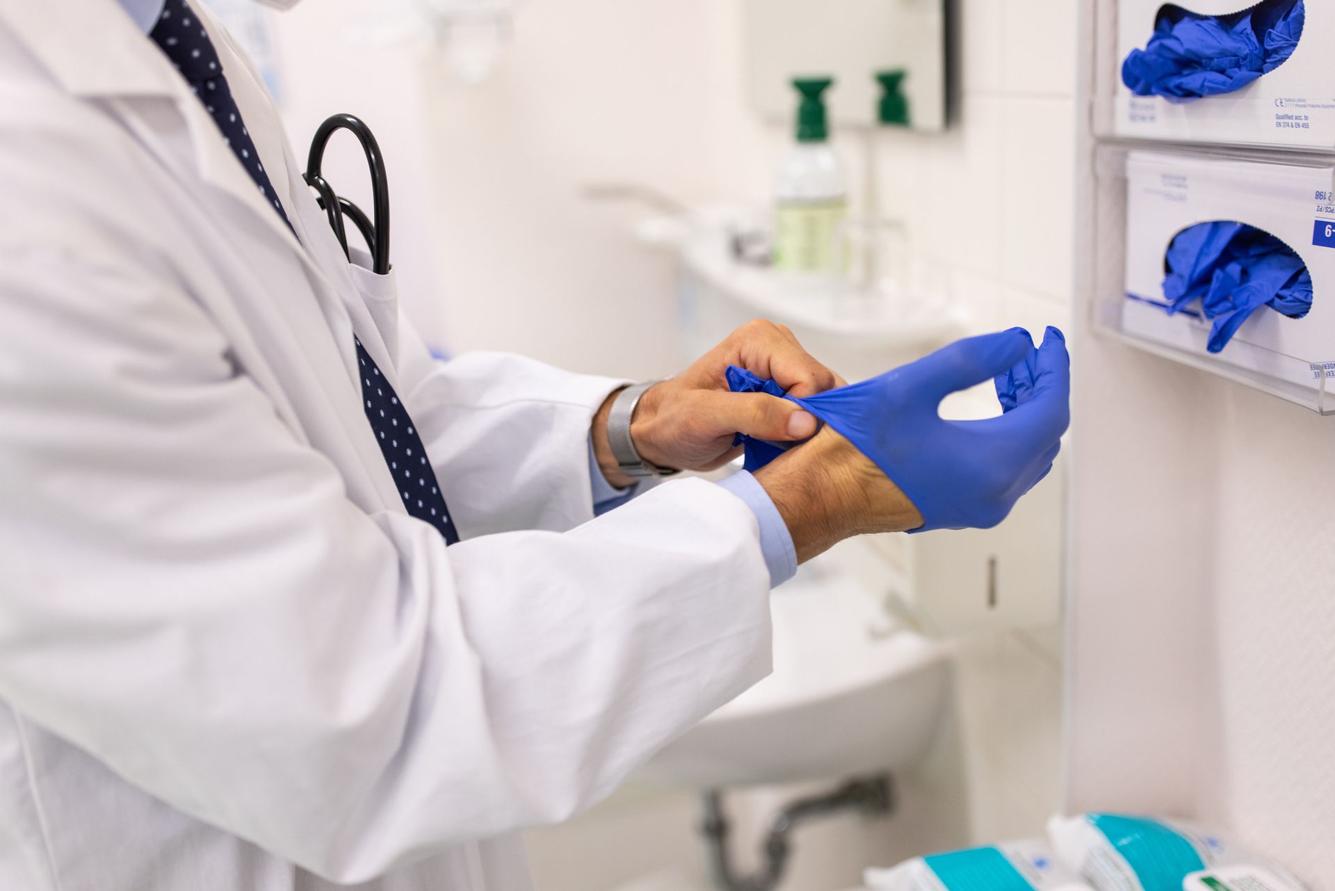Doctor in a white coat putting on blue medical gloves in an exam room. Doctor in a white coat putting on blue medical gloves in an exam room.