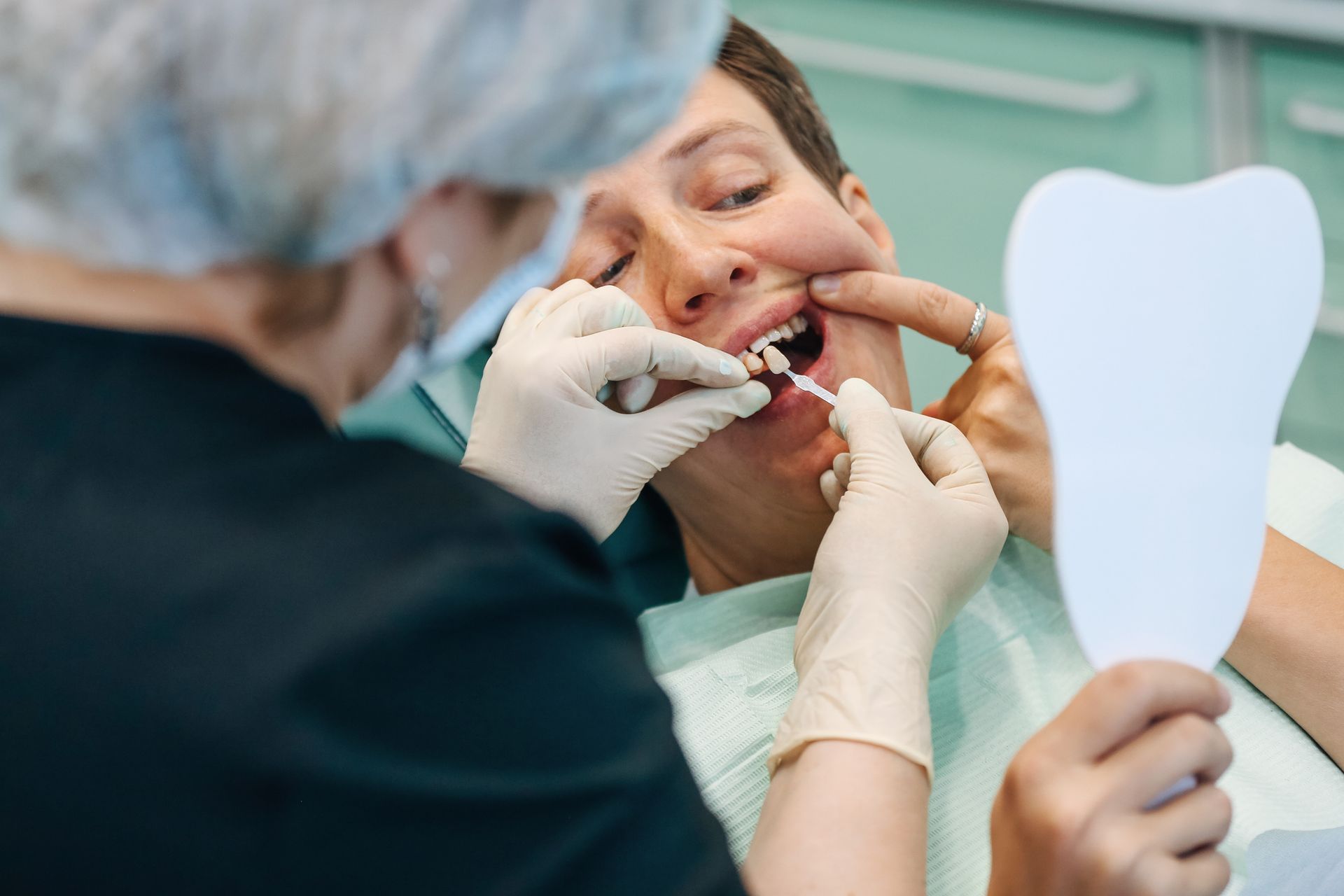 Dentist examining patient's teeth with color samples and a mirror in a dental office. Dentist examining patient's teeth with color samples and a mirror in a dental office.