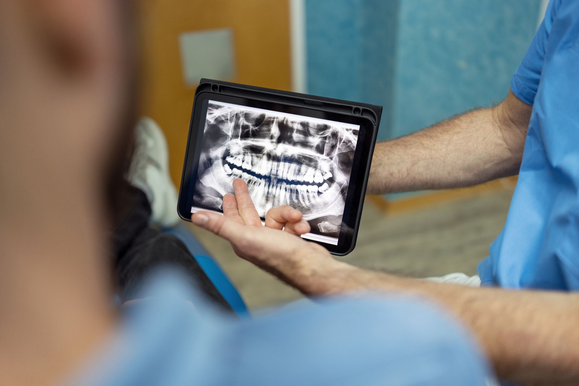 Dentist pointing to teeth X-ray on tablet screen, explaining to a patient in dental office. Dentist pointing to teeth X-ray on tablet screen, explaining to a patient in dental office.