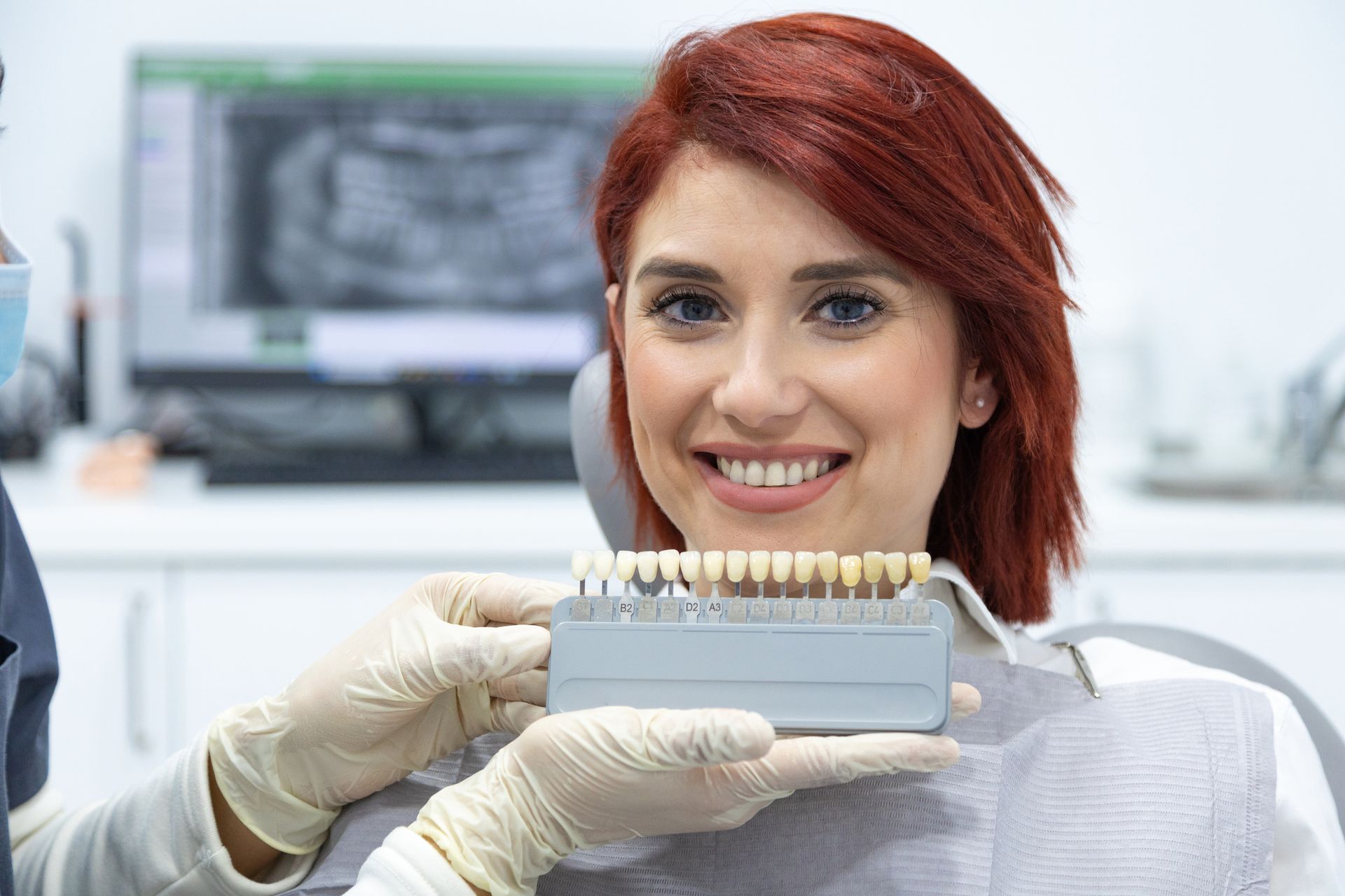 Woman in dental chair smiles while dentist holds teeth shade guide. Clinic setting. Woman in dental chair smiles while dentist holds teeth shade guide. Clinic setting.