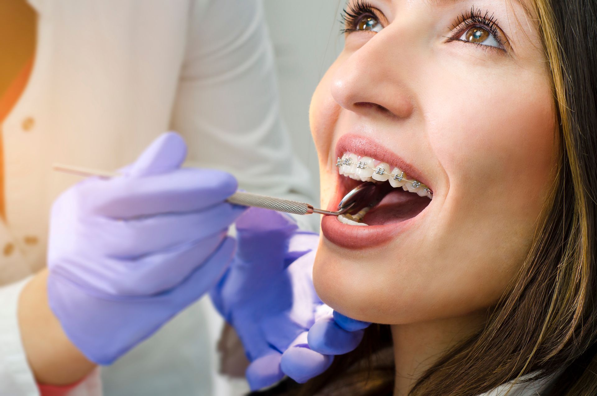 Dentist examining a patient's mouth with braces; wearing blue gloves.