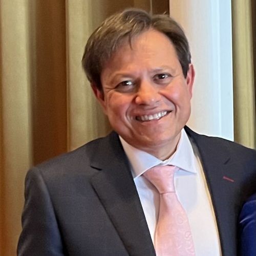 Man in a suit smiles, wearing a pink tie.