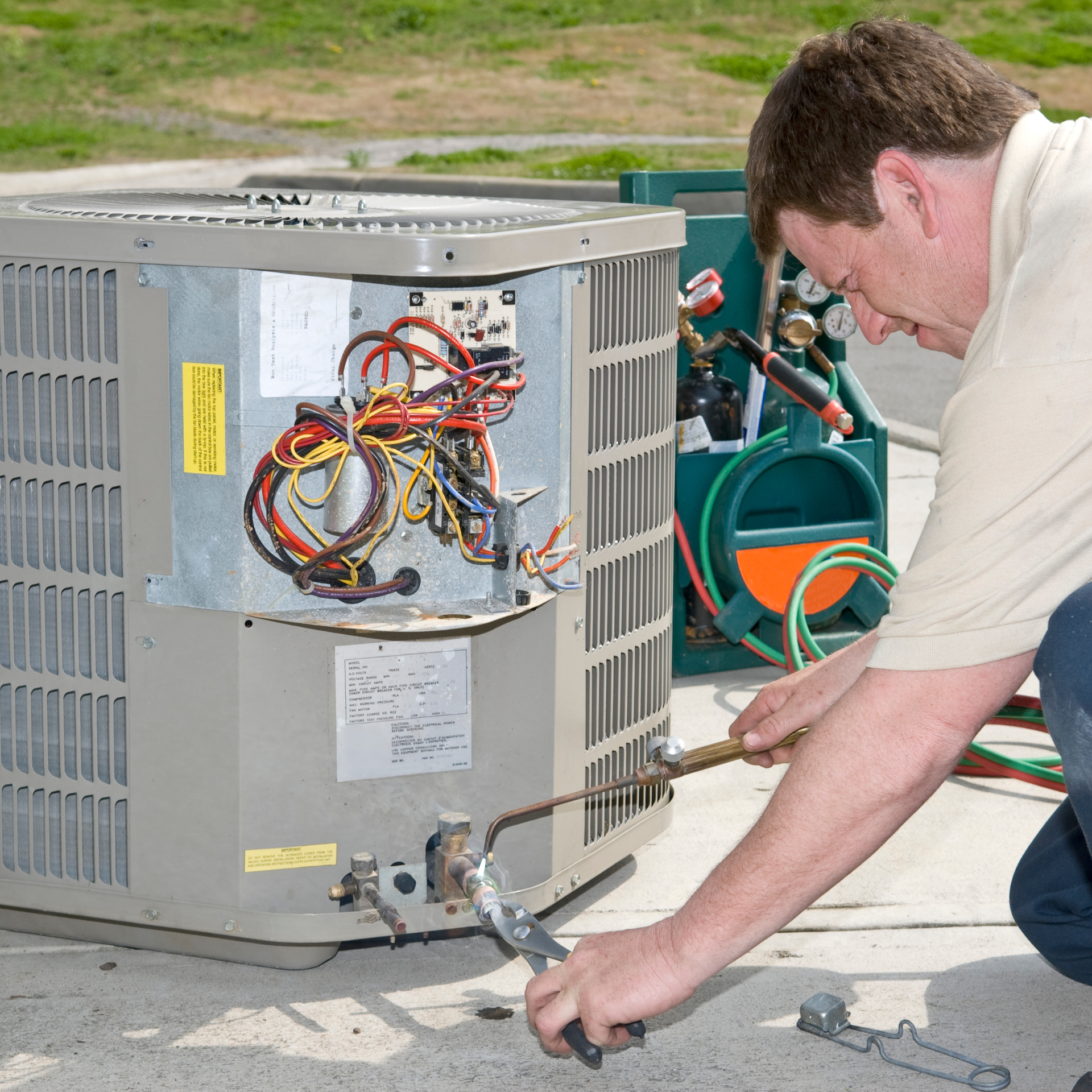Man repairing an air conditioning unit outdoors with a torch, using tools.