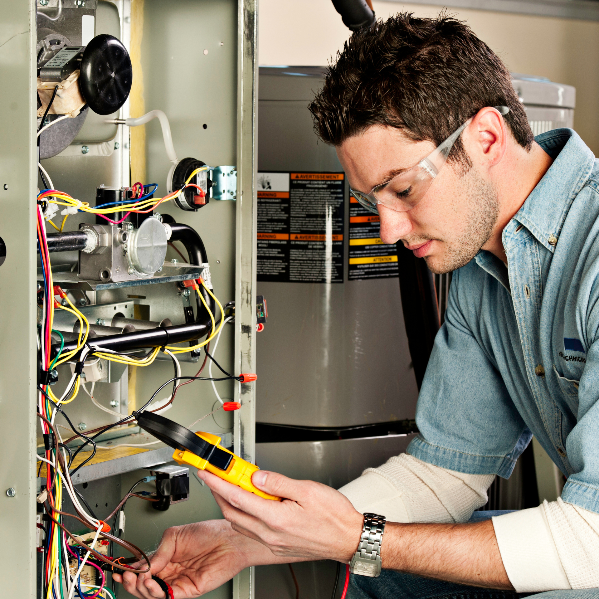 Man with safety glasses using a multimeter to inspect an electrical panel.