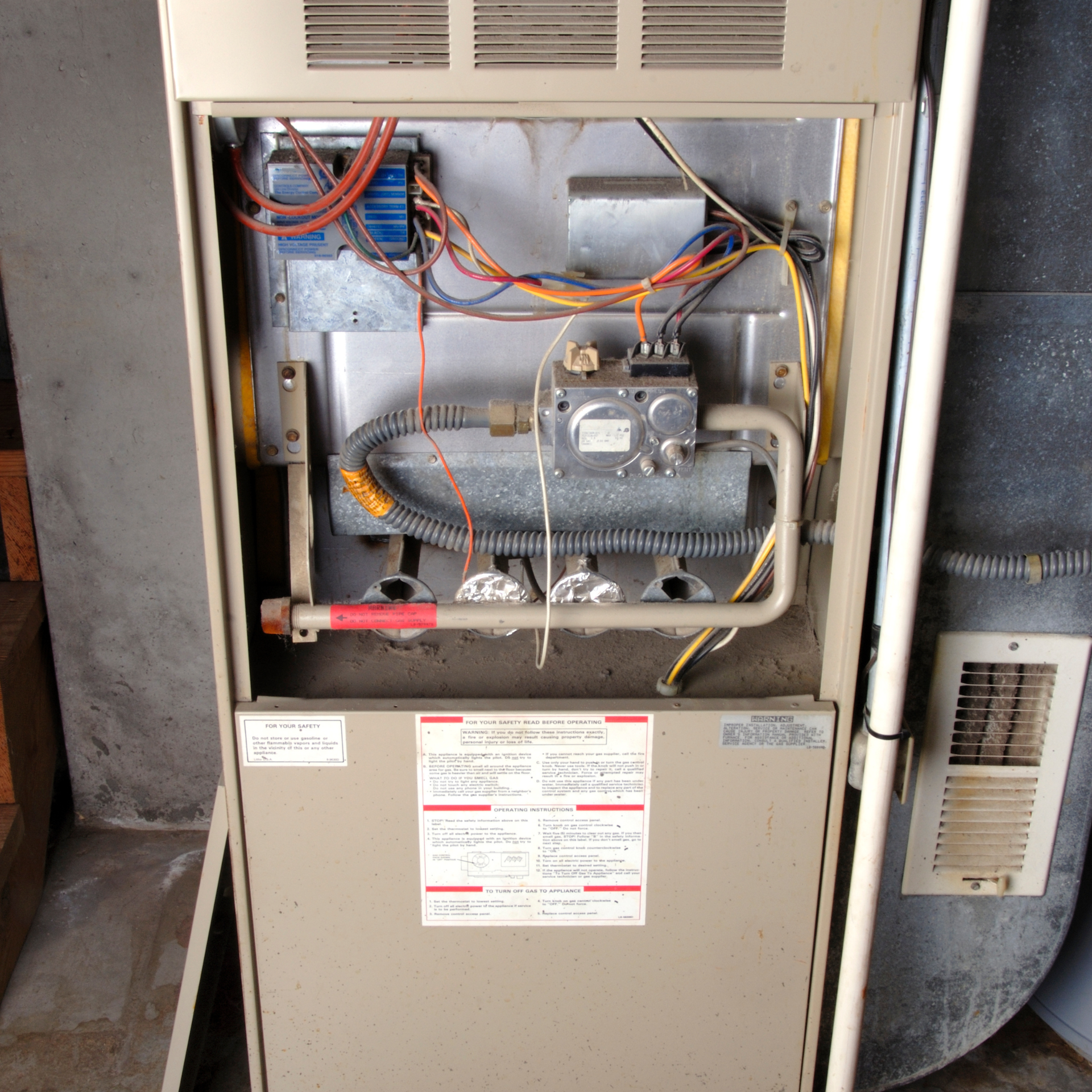 Open view of a gas furnace showing electrical components, gas valve, and burners. Beige and silver metal.