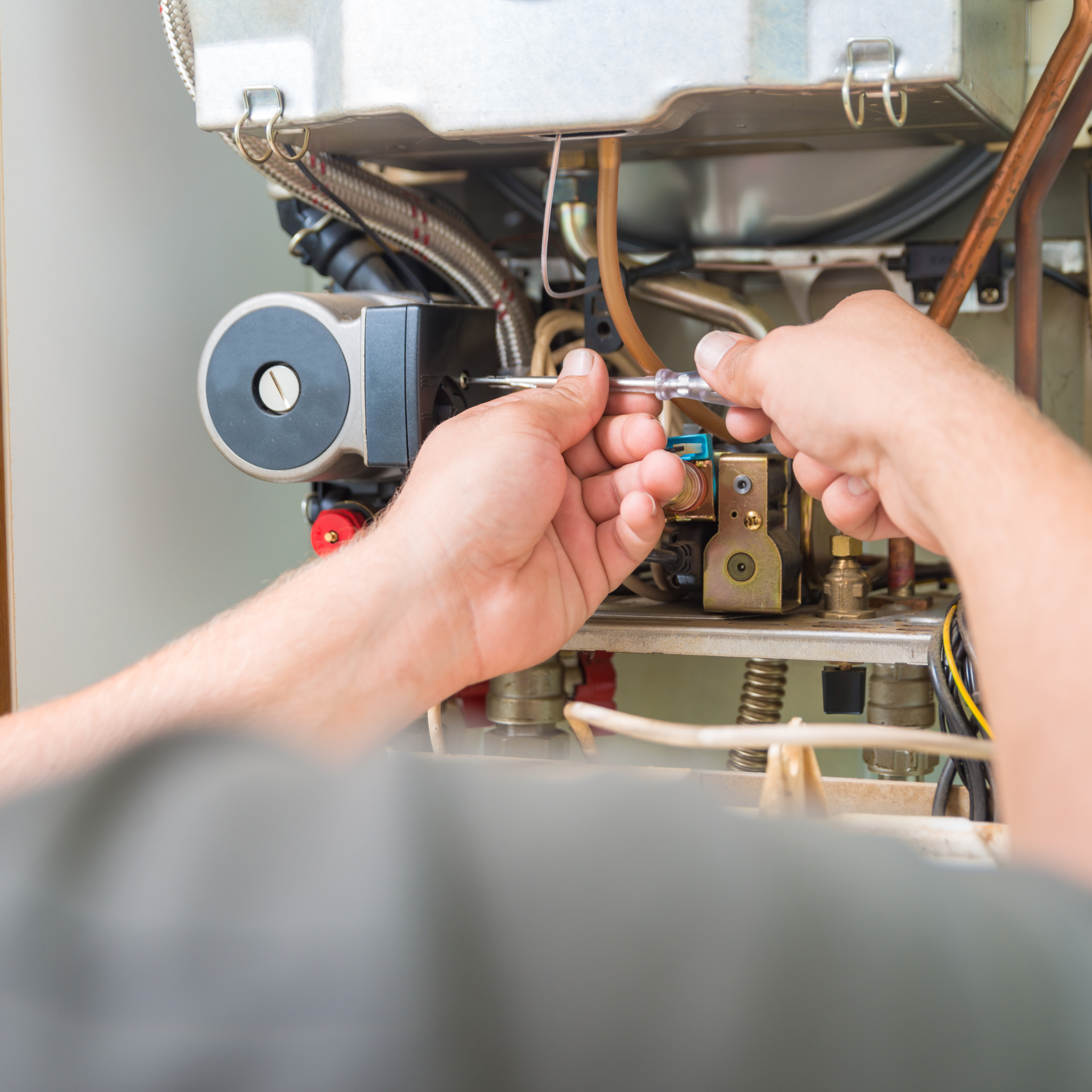 Person using a screwdriver to work on a furnace or boiler.