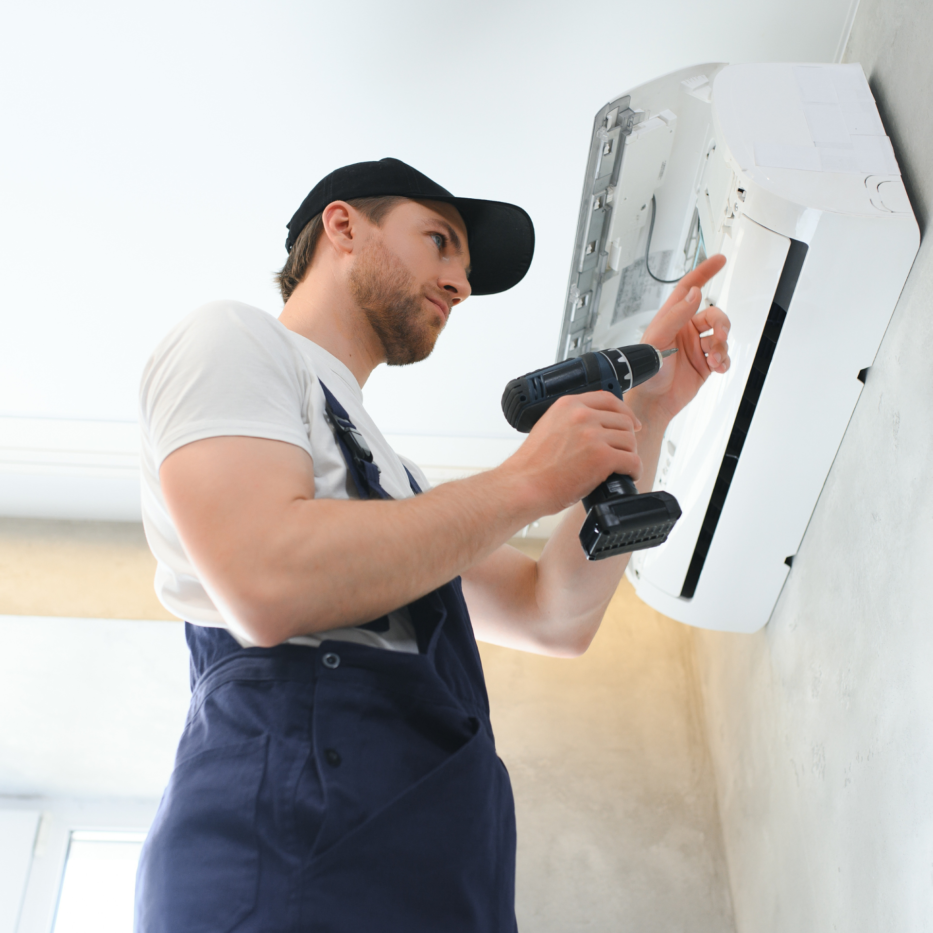 Person in overalls installing air conditioner with a drill.