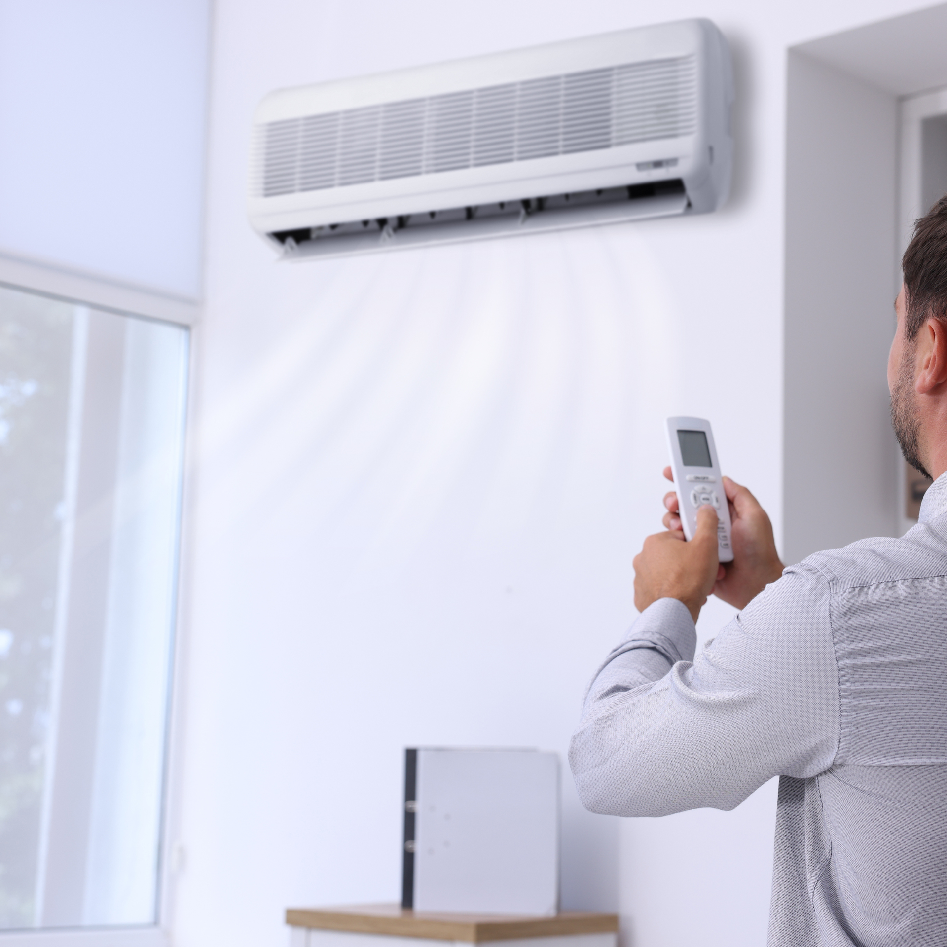Person using a remote control to operate a wall-mounted air conditioner in a room.