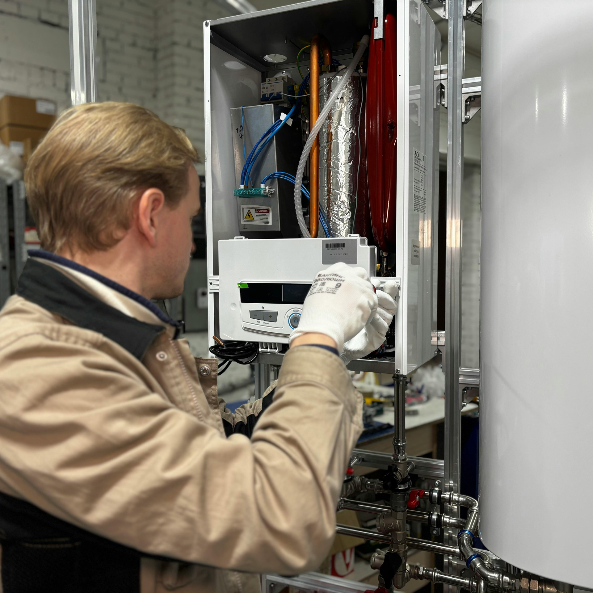 Man in work clothes inspecting a boiler with white gloves on in a workshop.