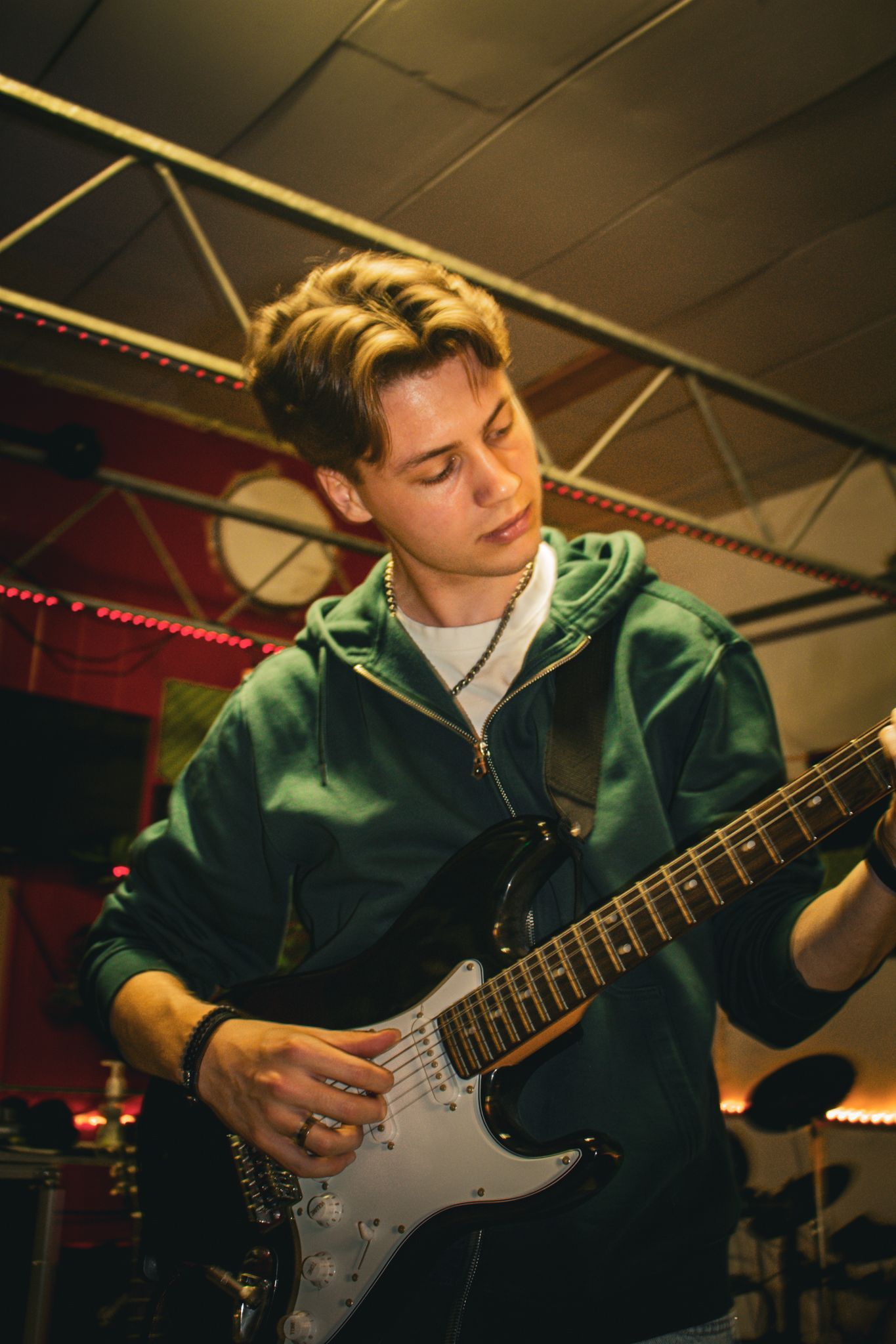 Een jongeman in een groene hoodie speelt op een elektrische gitaar.