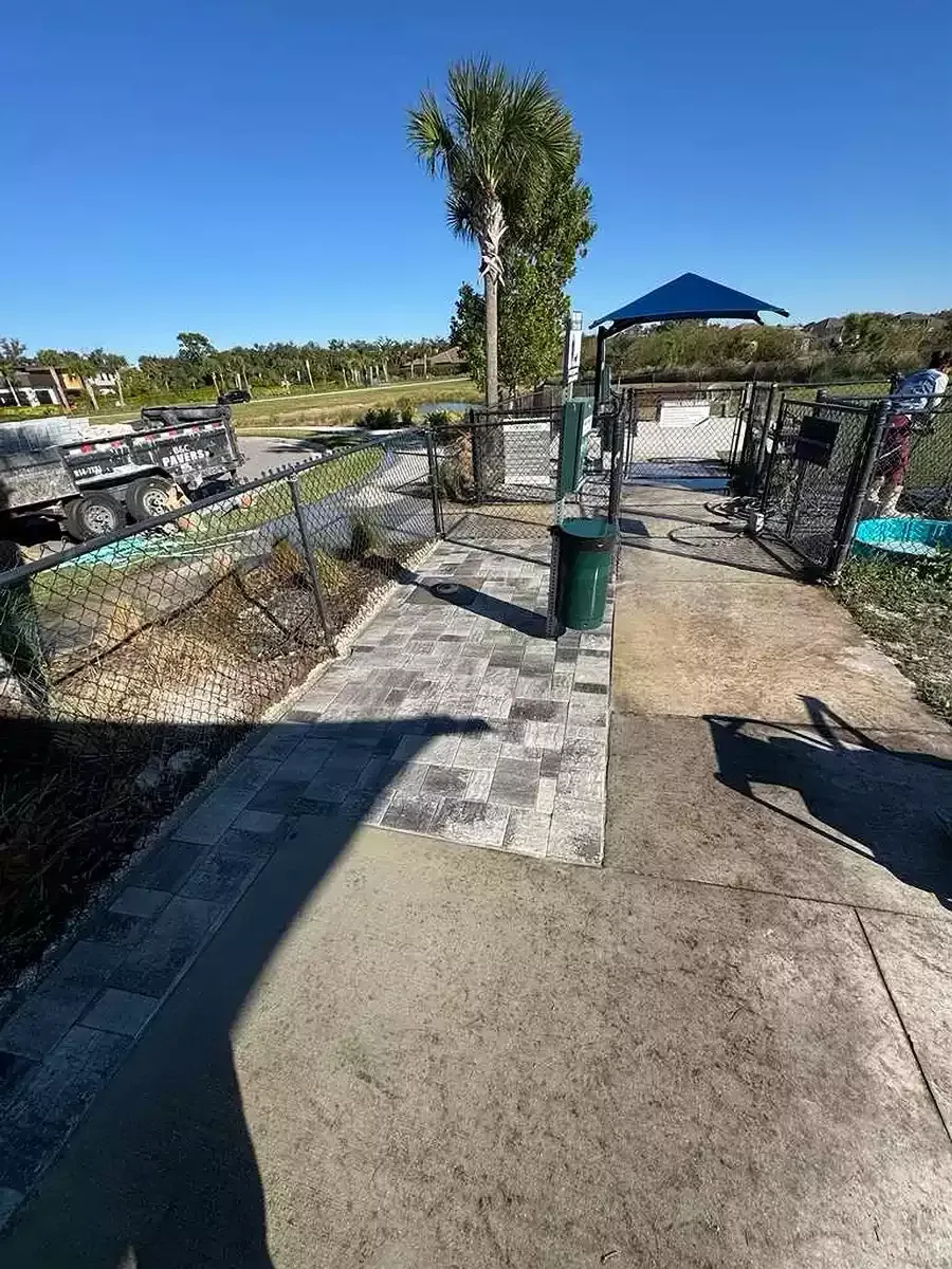 Gray concrete paver walkway beside fenced commercial dog park entrance