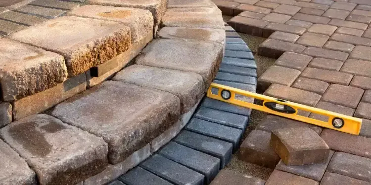 Curved concrete paver step with dark border and leveling tool during installation