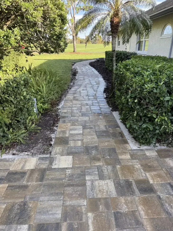 Curved concrete paver walkway beside residential home and landscaping