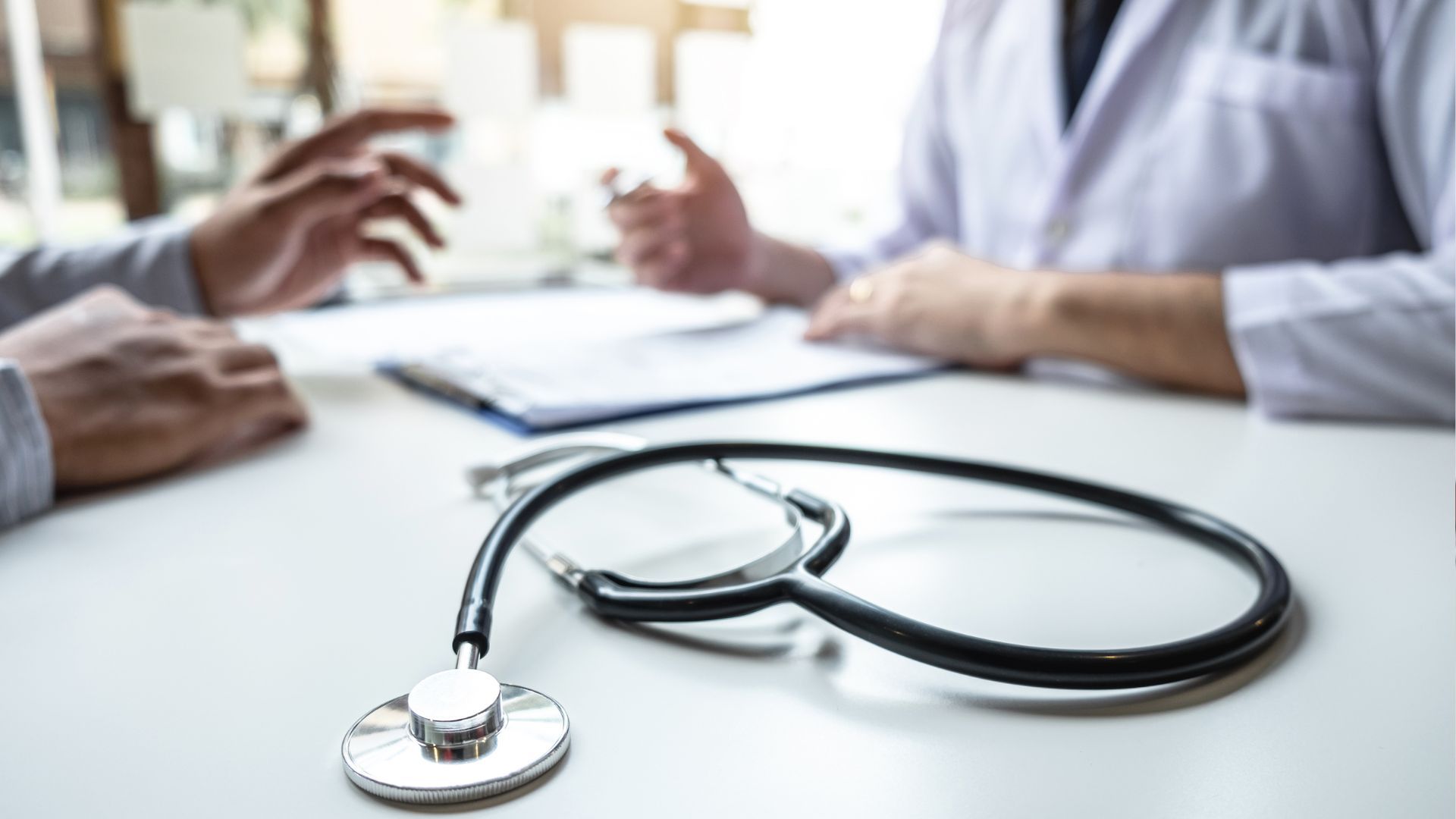 A stethoscope is sitting on a table next to a doctor and a patient.
