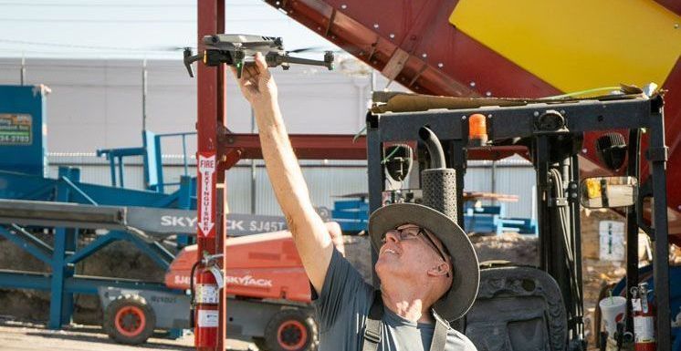 Photo by Phoenix Drone Pros, Robert Biggs, A man in a hat is holding up a drone in front of a forklift.