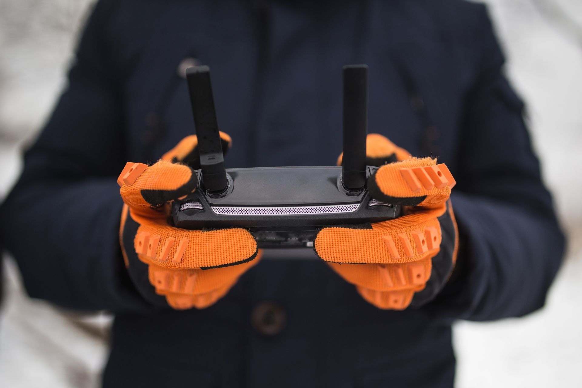 A person wearing orange gloves is holding a remote control in their hands.