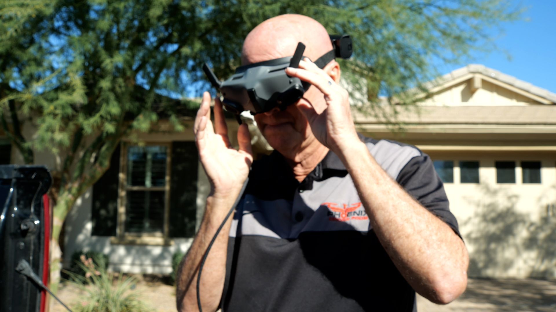 Photo by Phoenix Drone Pros, Robert Biggs, A man wearing a virtual reality headset is standing in front of a house.