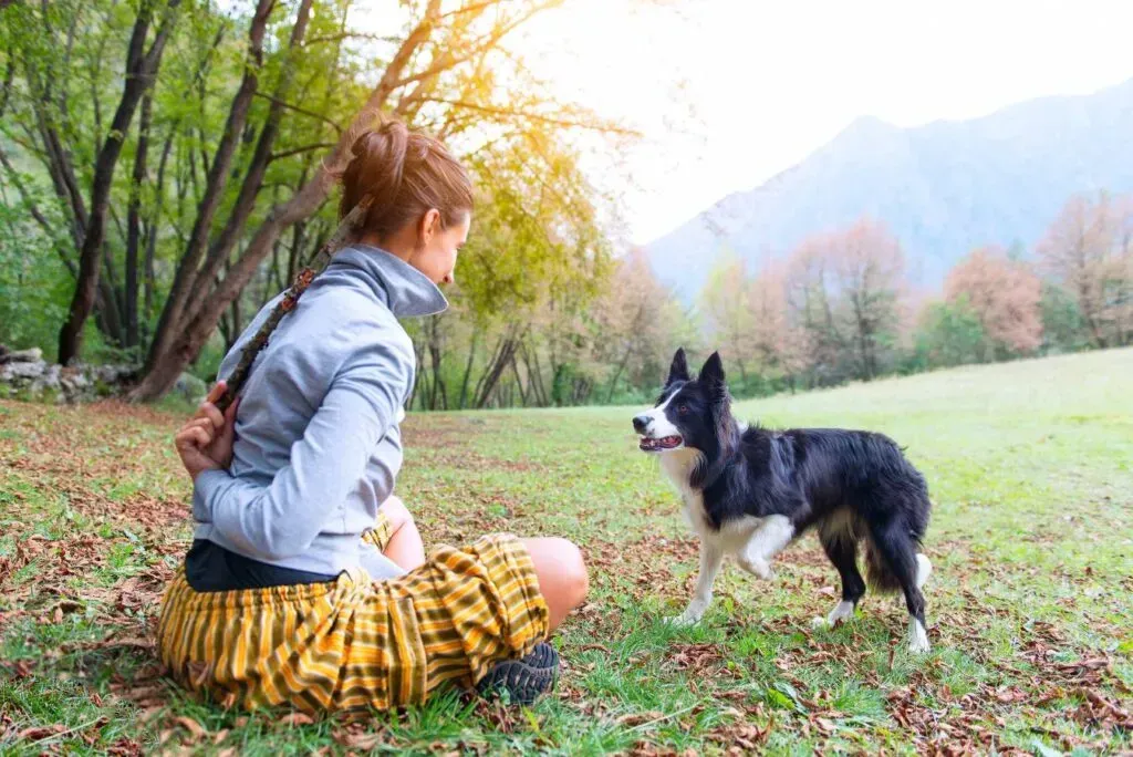 A woman is sitting on the grass with her dog.