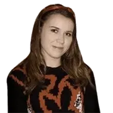 A young woman wearing a black and red sweater and a headband is standing in front of a white background.