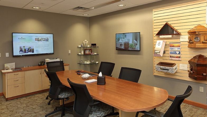 A conference room with a long wooden table and chairs and a flat screen tv.