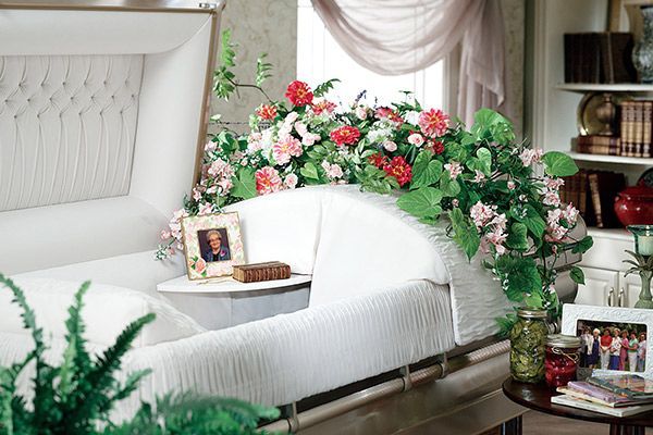 a white coffin in a living room with flowers on it