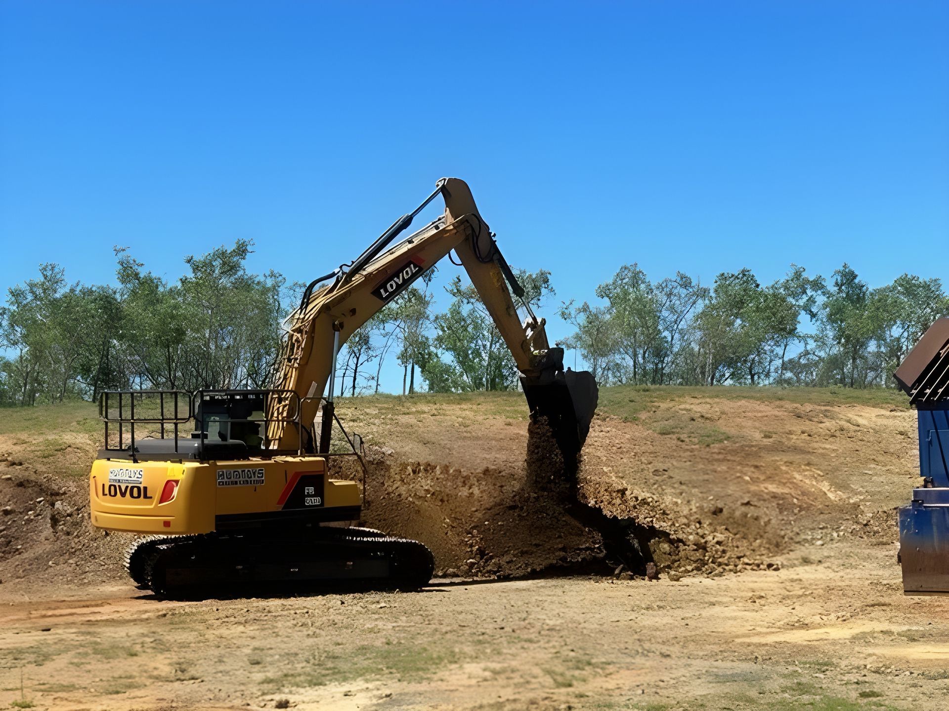 Yellow Excavator Digging Into a Dirt Mound Under a Blue Sky — Huntlys Heavy Equipment in Central Highlands, QLD