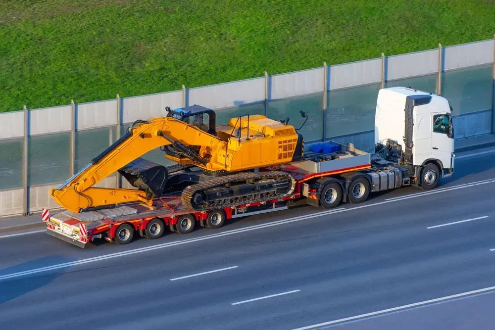 Yellow Excavator on a Flatbed Trailer Towed by a White Semi-truck on a Highway — Huntlys Heavy Equipment In Gracemere, QLD