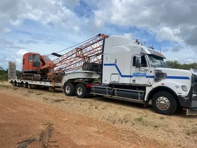 White Semi-truck Carrying an Orange Excavator and Crane Boom on a Flatbed — Huntlys Heavy Equipment In Gracemere, QLD