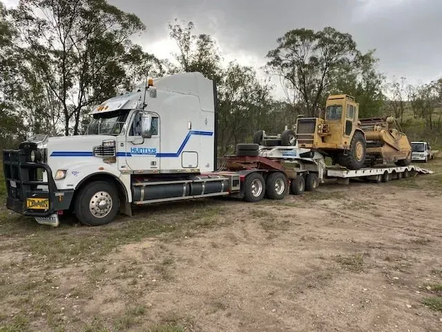 White Semi-truck Transporting a Yellow Bulldozer on a Flatbed Trailer — Huntlys Heavy Equipment In Gracemere, QLD