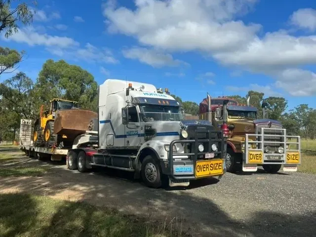 Two Semi-trucks Parked Outdoors, One Hauling Yellow Construction Equipment — Huntlys Heavy Equipment In Gracemere, QLD