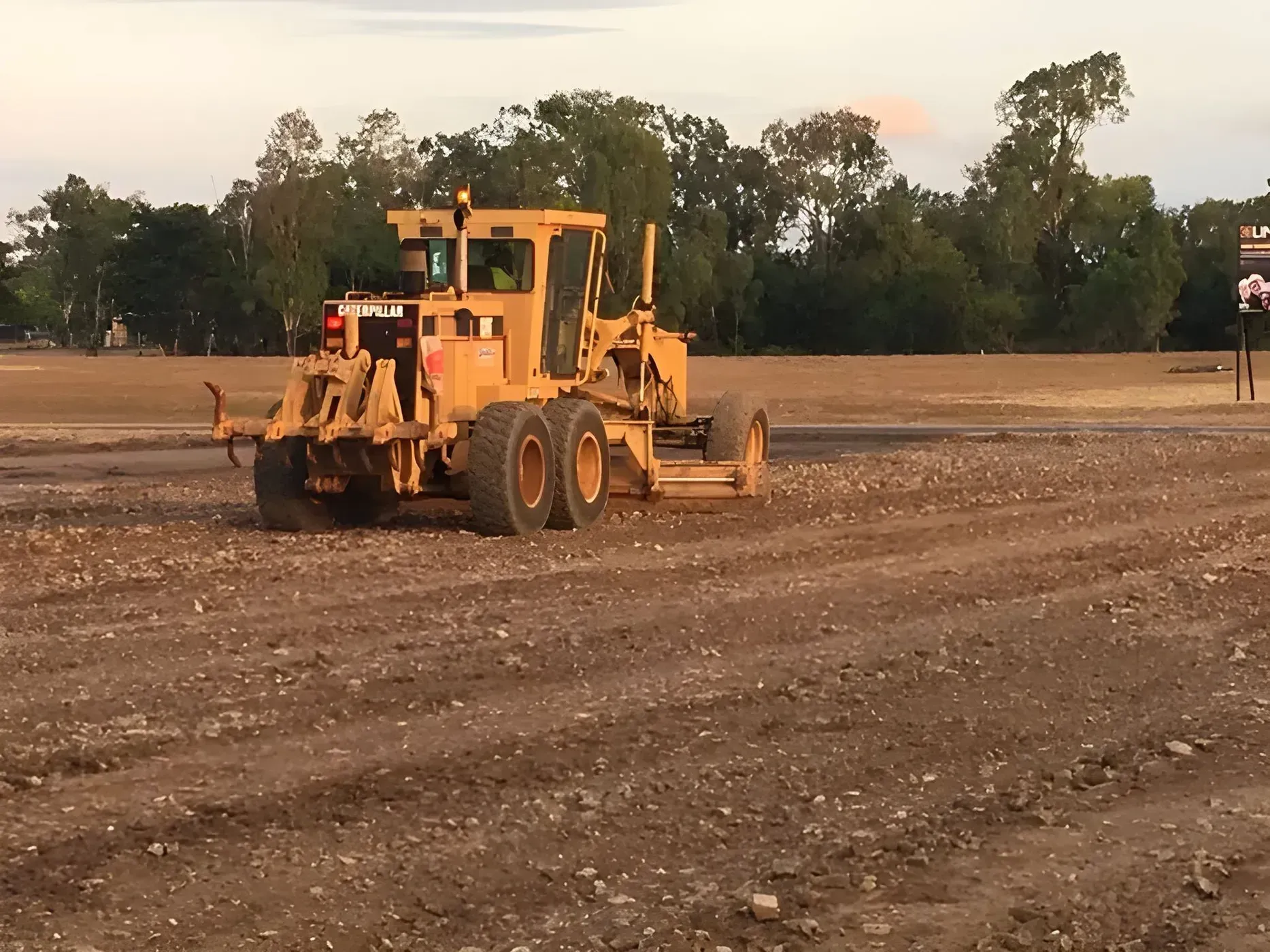 Yellow Grader Smoothing a Gravel Surface in an Open Area — Huntlys Heavy Equipment In Gracemere, QLD