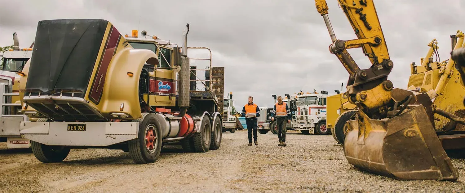 Two People in Orange Vests Walk Through a Lot of Heavy Machinery — Huntlys Heavy Equipment In Gracemere, QLD