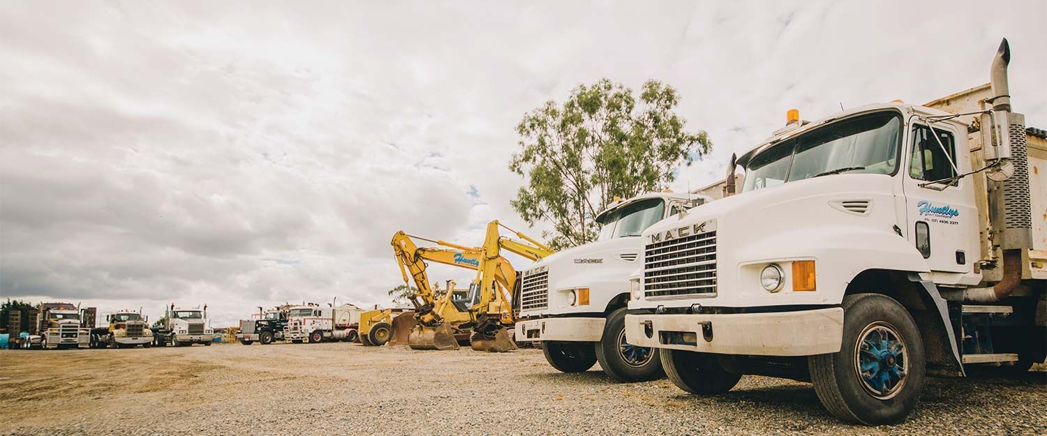 Fleet of White Construction Trucks and Yellow Excavators Parked on a Gravel — Huntlys Heavy Equipment in Gracemere, QLD