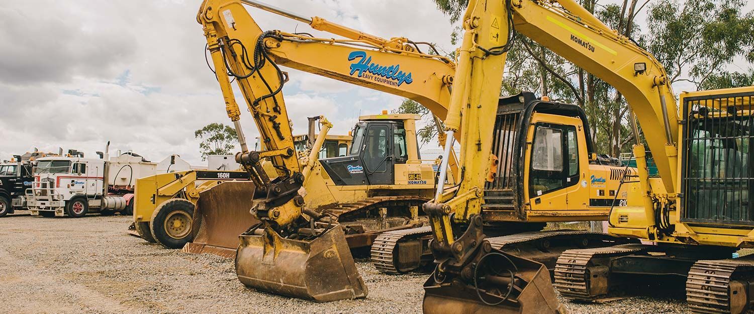 Yellow Construction Equipment Parked on Gravel Under a Cloudy Sky — Huntlys Heavy Equipment In Gracemere, QLD