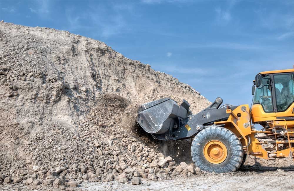 Yellow Front-end Loader Scoops Dirt From a Large Pile Under a Blue Sky — Huntlys Heavy Equipment in Yeppoon, QLD