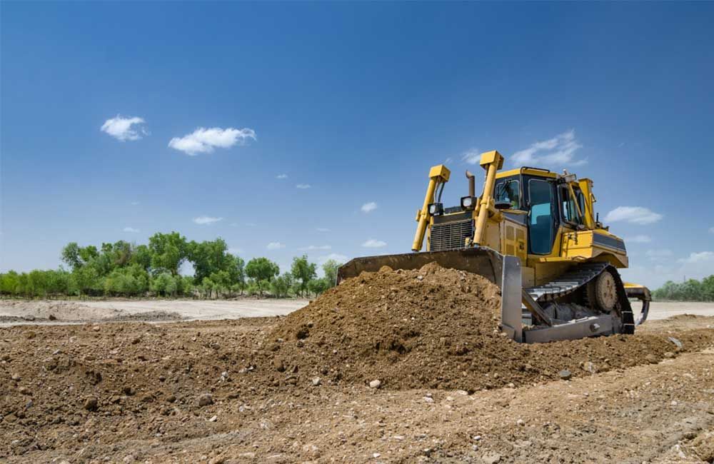 Yellow Bulldozer Pushing Dirt Across a Construction Site Under a Blue Sky — Huntlys Heavy Equipment in Gladstone, QLD