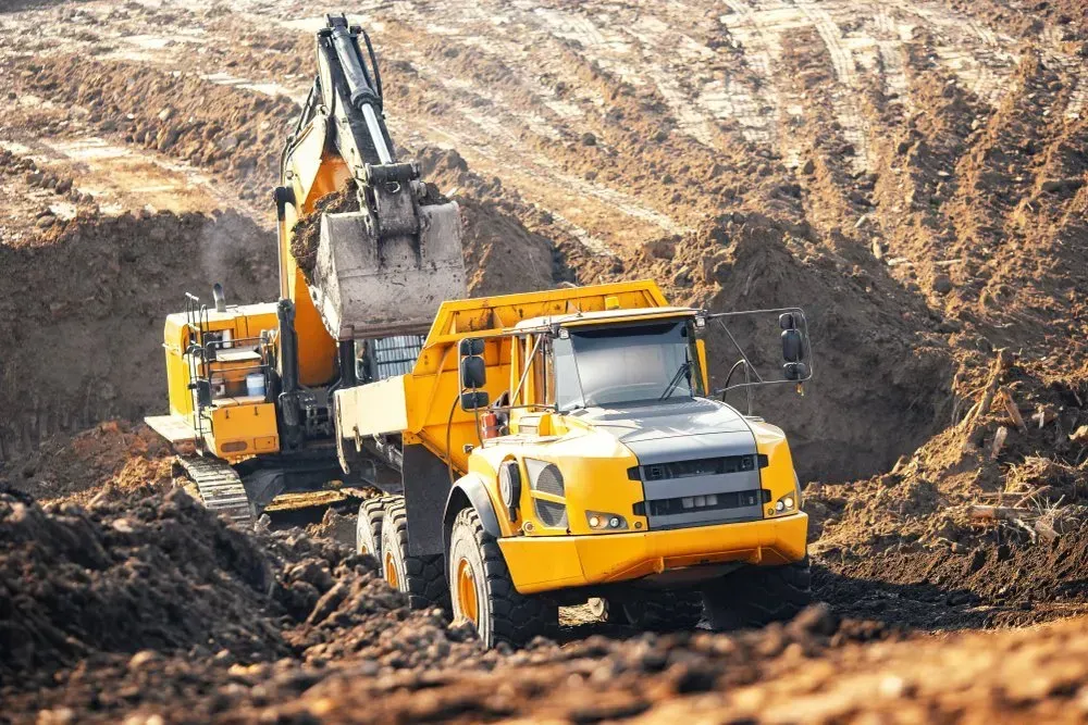 Yellow Excavator Loading a Yellow Dump Truck With Soil at a Construction Site — Huntlys Heavy Equipment In Gracemere, QLD