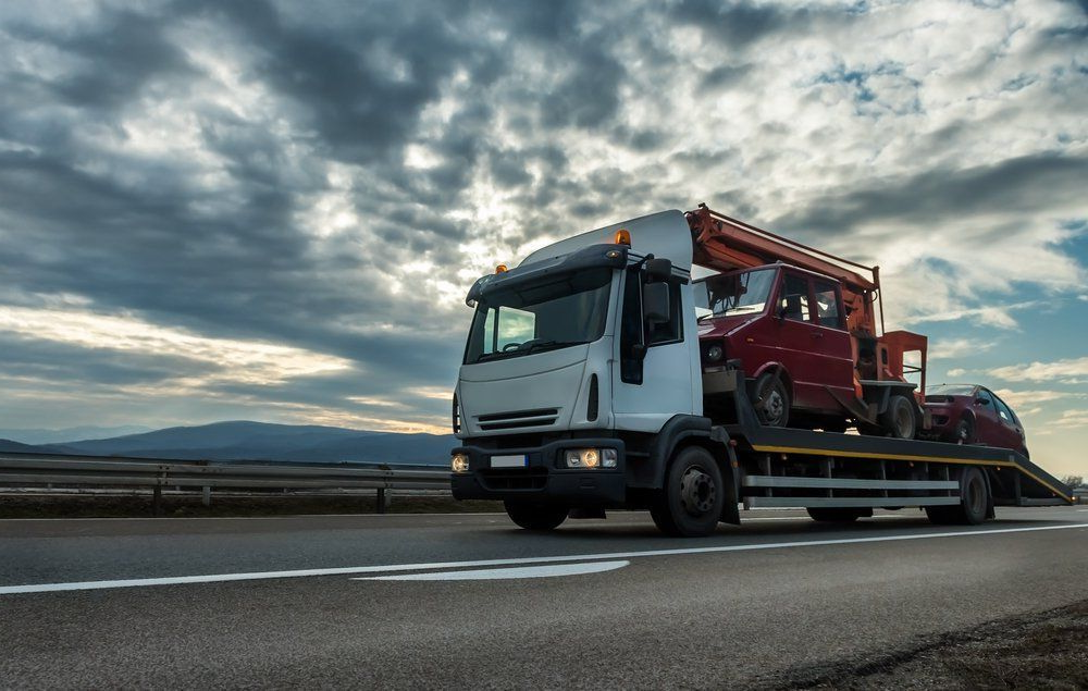 Tow Truck Carrying a Red Car on a Highway Under a Cloudy Sky — Huntlys Heavy Equipment in Gracemere, QLD